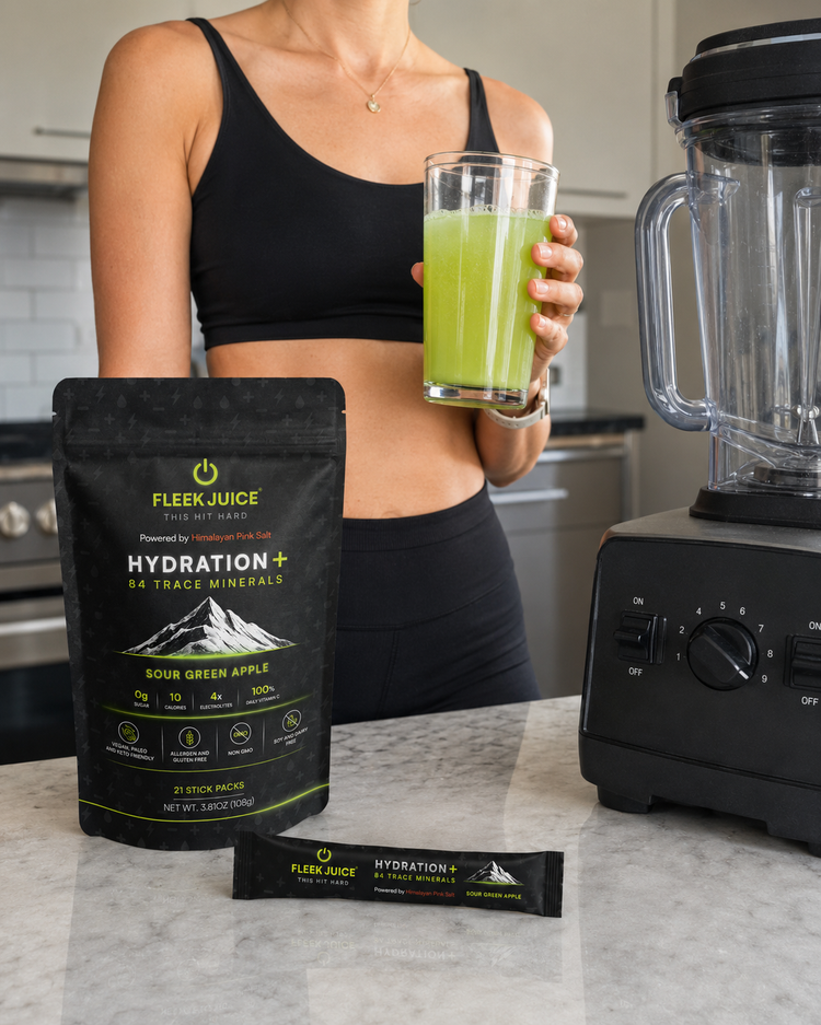 Woman in fitness wear holding green hydration drink, Fleek Juice supplement pack on counter, blender nearby.