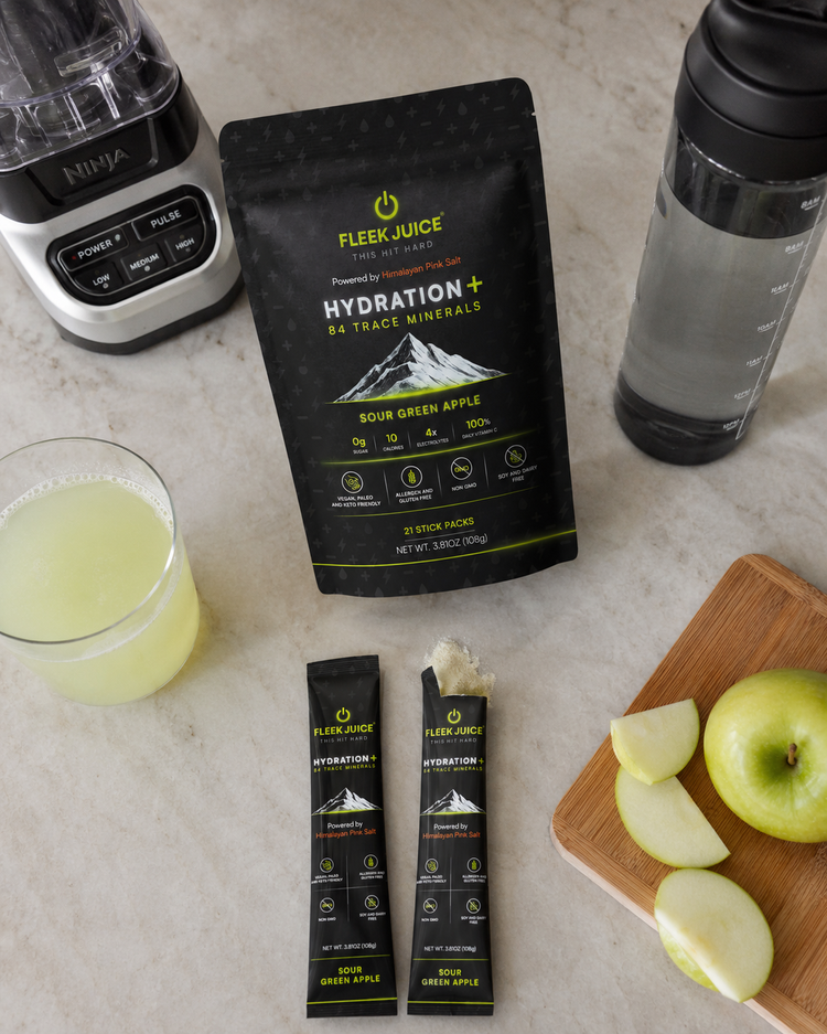Hydration drink mix with sour green apple flavor, sliced apples, blender, and water bottle on kitchen counter