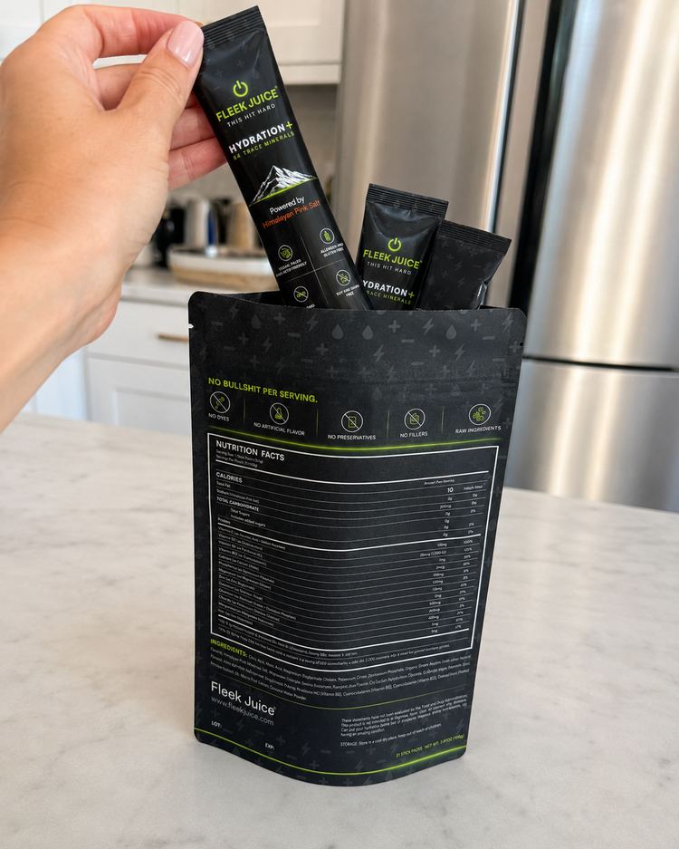 Hand holding Fleek Juice Hydration+ supplement stick above product pouch on kitchen counter