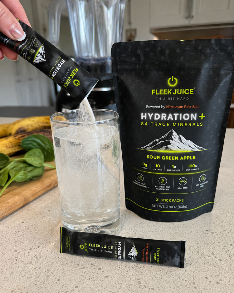 Pouring Fleek Juice Hydration+ sour green apple stick pack into a glass of water on kitchen counter