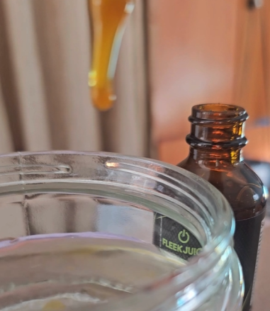 Glass dropper with supplement liquid above water jar and amber bottle labeled FLEEK JUICE.