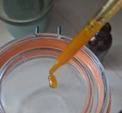 Close-up of amber liquid supplement dropper above glass jar