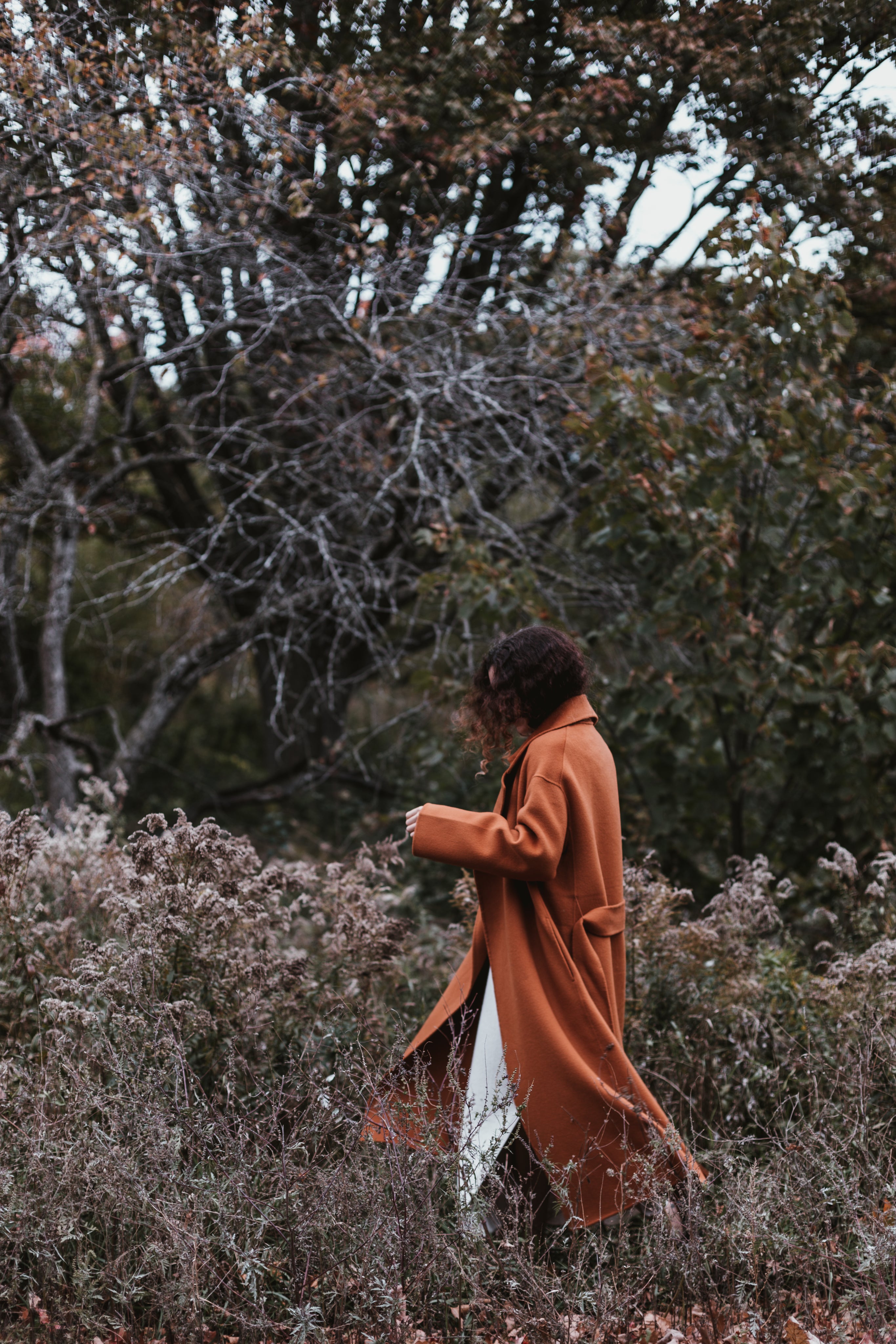Young woman in an autumn-colored coat walking through a forest with fall foliage